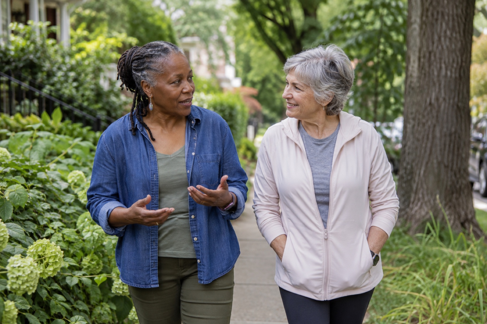 Two friends walk and talk along a leafy neighborhood path.